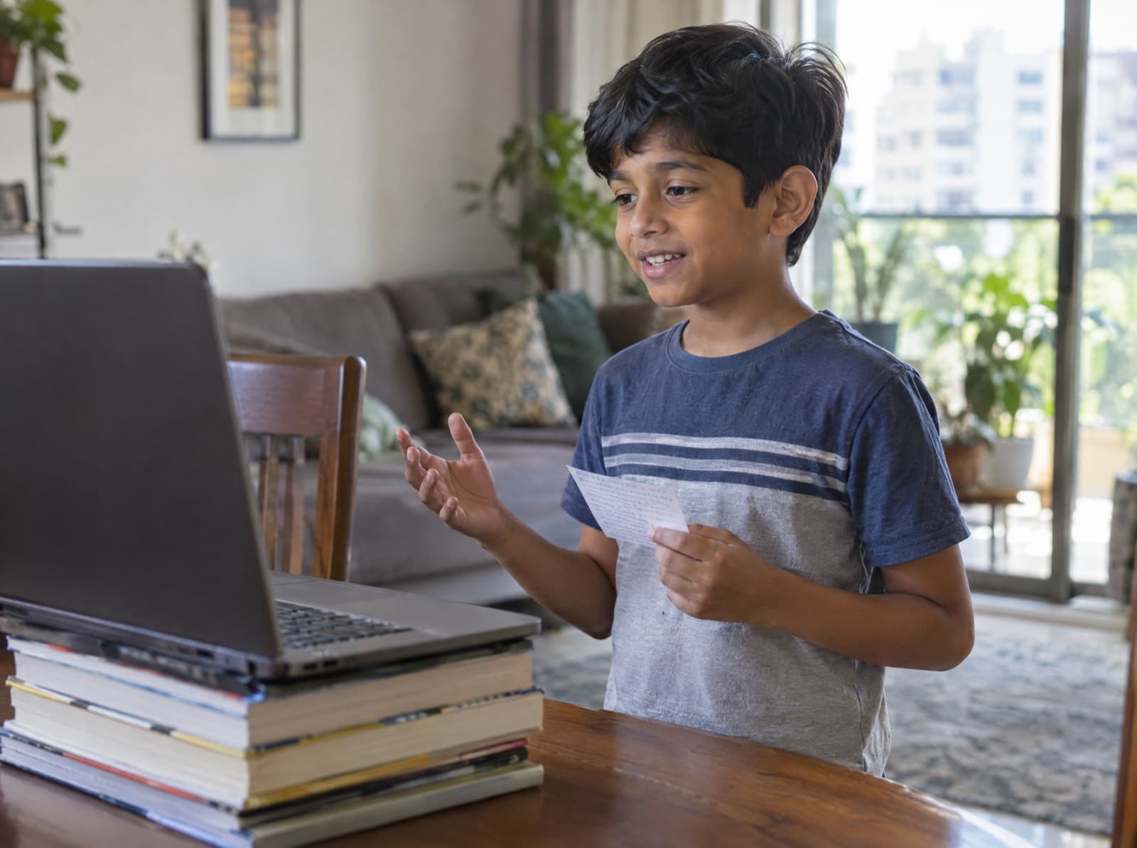 A boy of about nine speaks to his online class from the dining table, a note card in his hand.